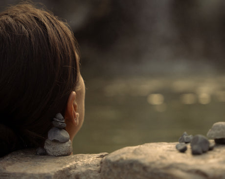 Femme de dos contemplant un lac près de galets empilés, moment de sérénité